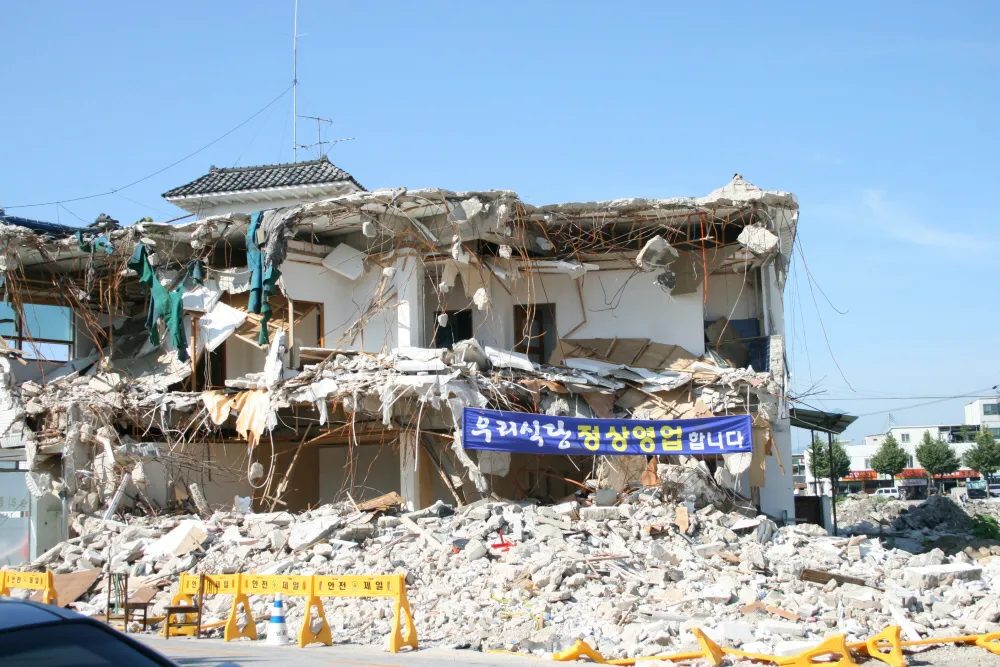 A half-demolished building with a banner reading "Open as usual"